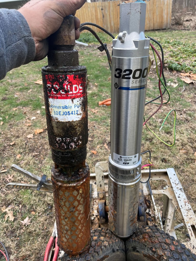 Hand holding rusty well pump next to stainless steel submersible well pump on outdoor metal frame