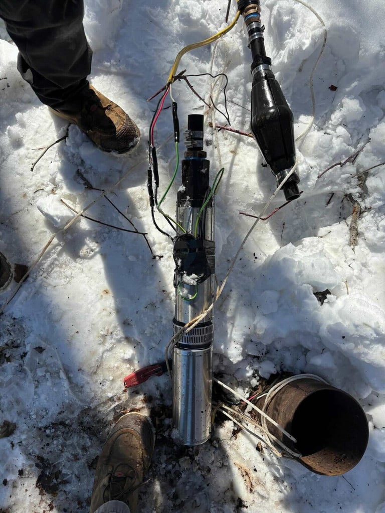 Overhead view of person holding ice fishing equipment including a rod, cables, and bucket in snow